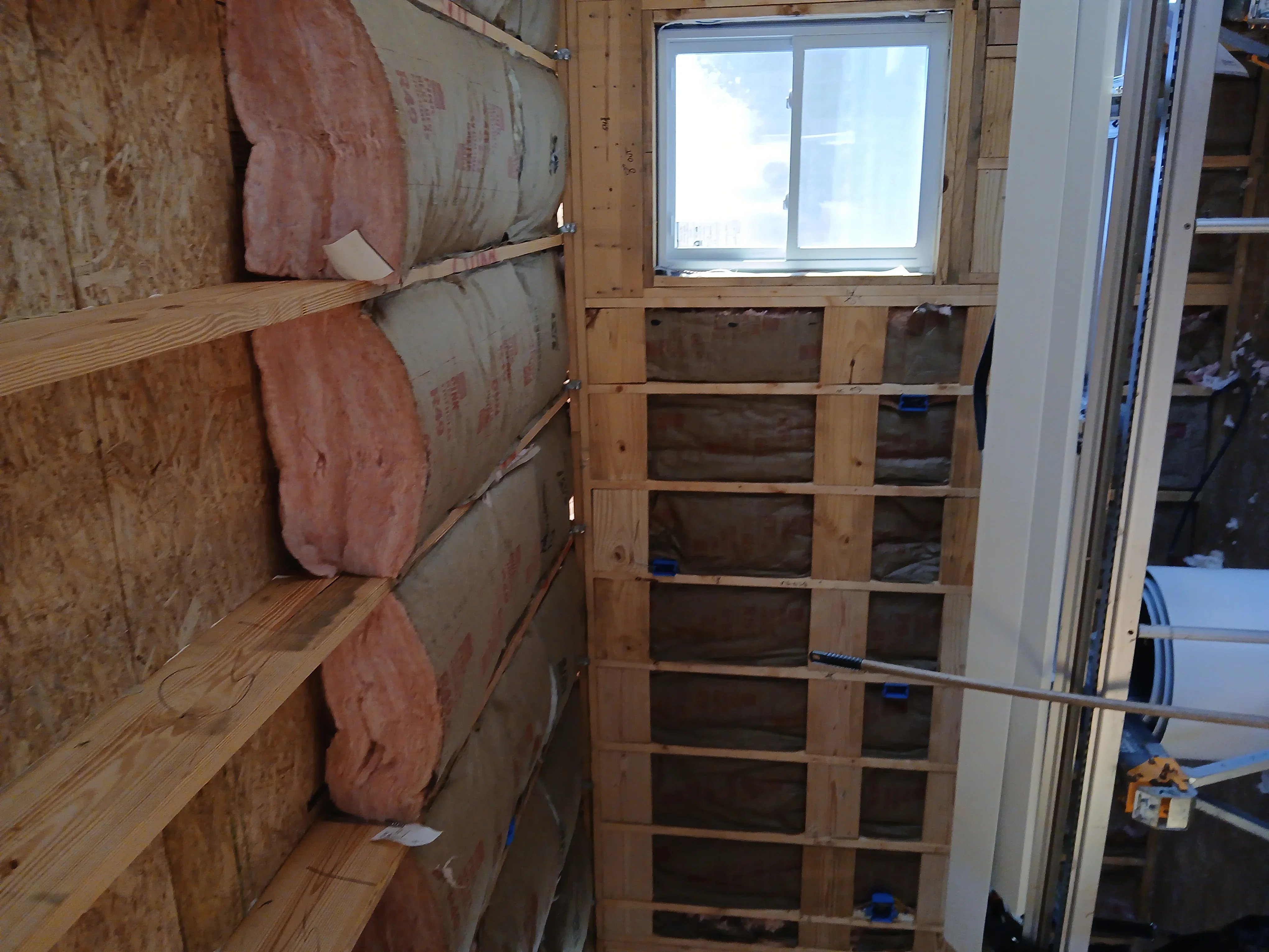 Fiberglass insulation batts on wooden framing with new double-pane window installation