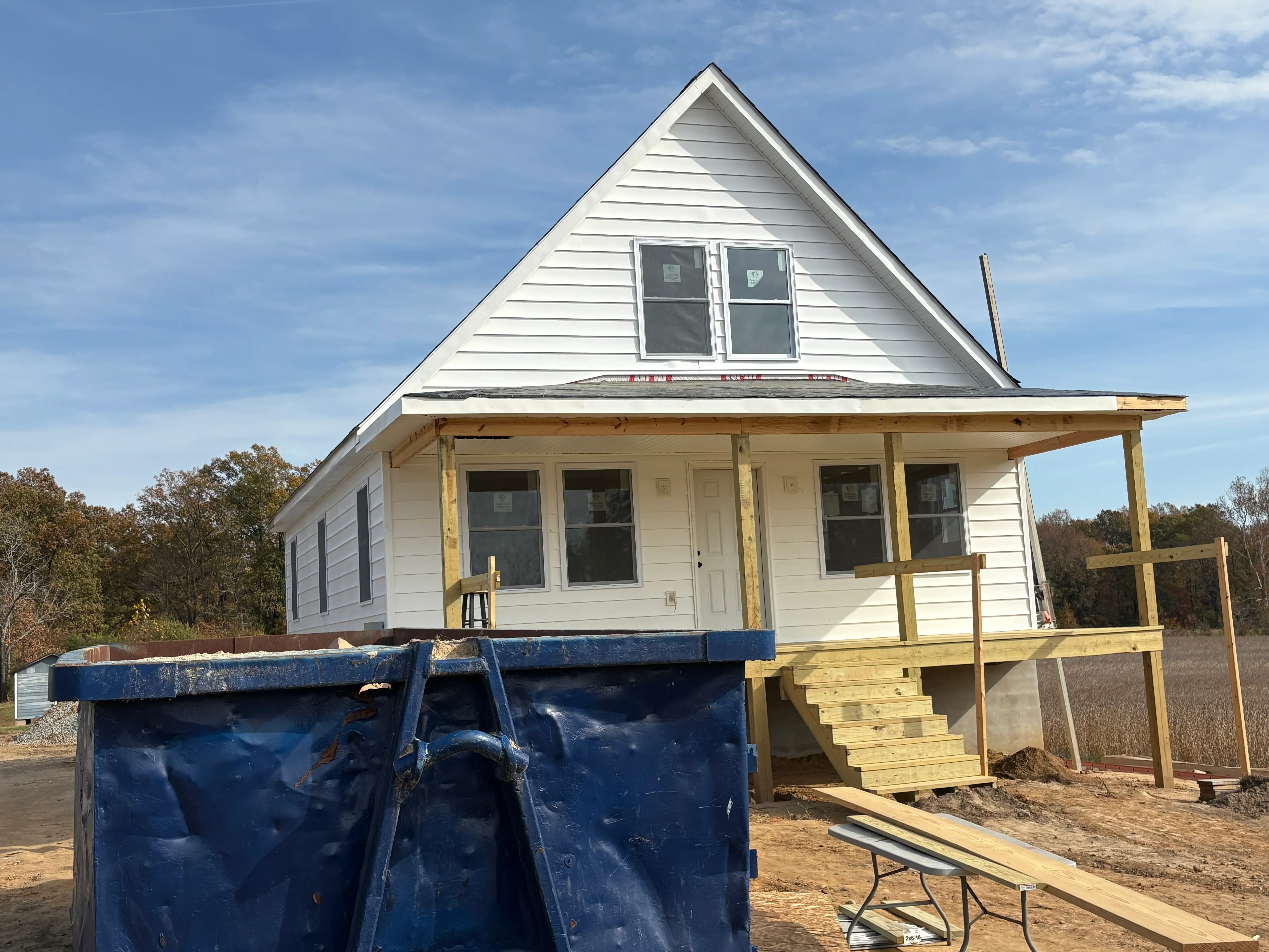 White lap siding home with new wooden porch framing and multi-pane windows under construction