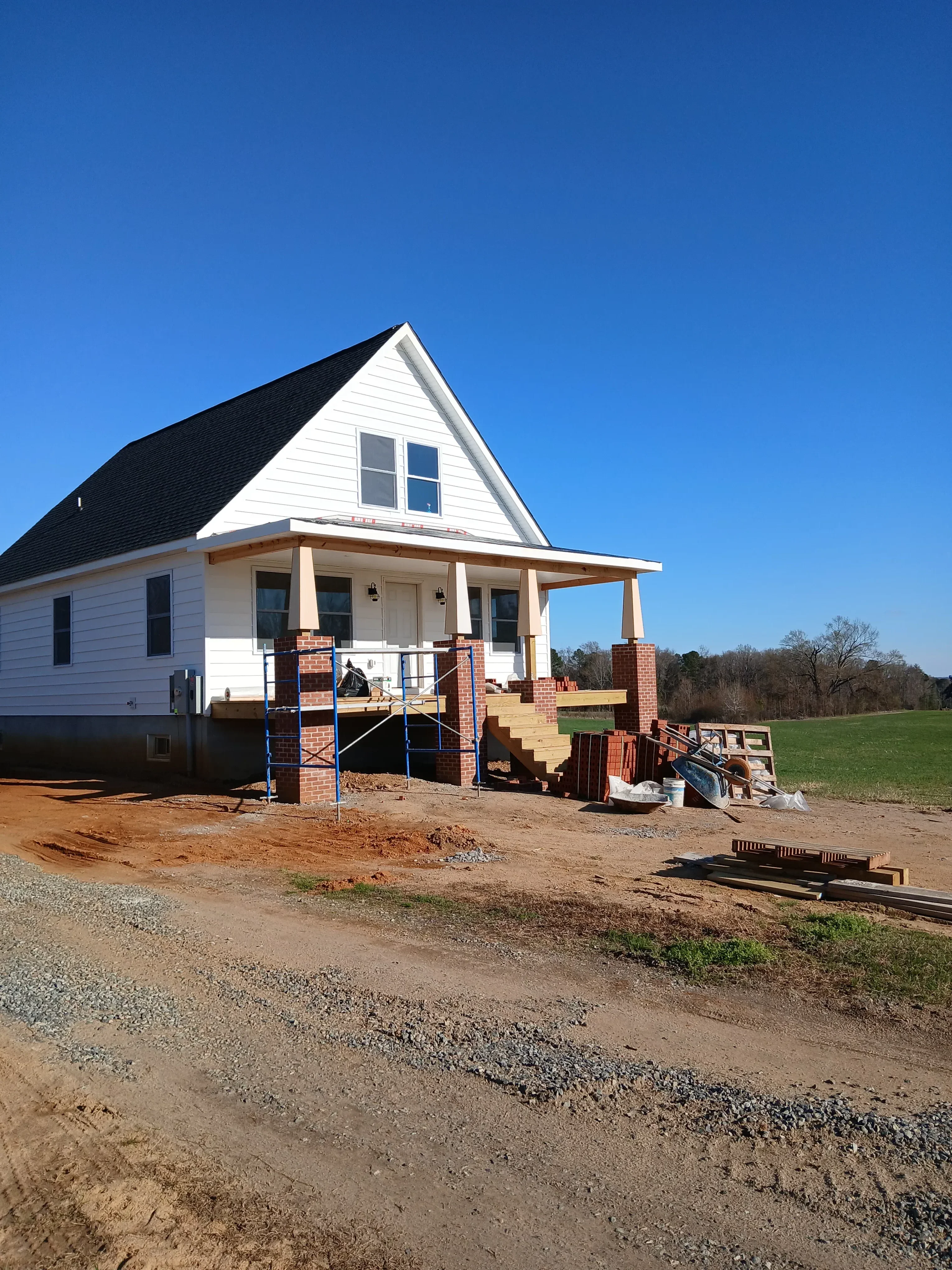 Residential construction with brick veneer addition, metal roof framing, and steel support beams under construction