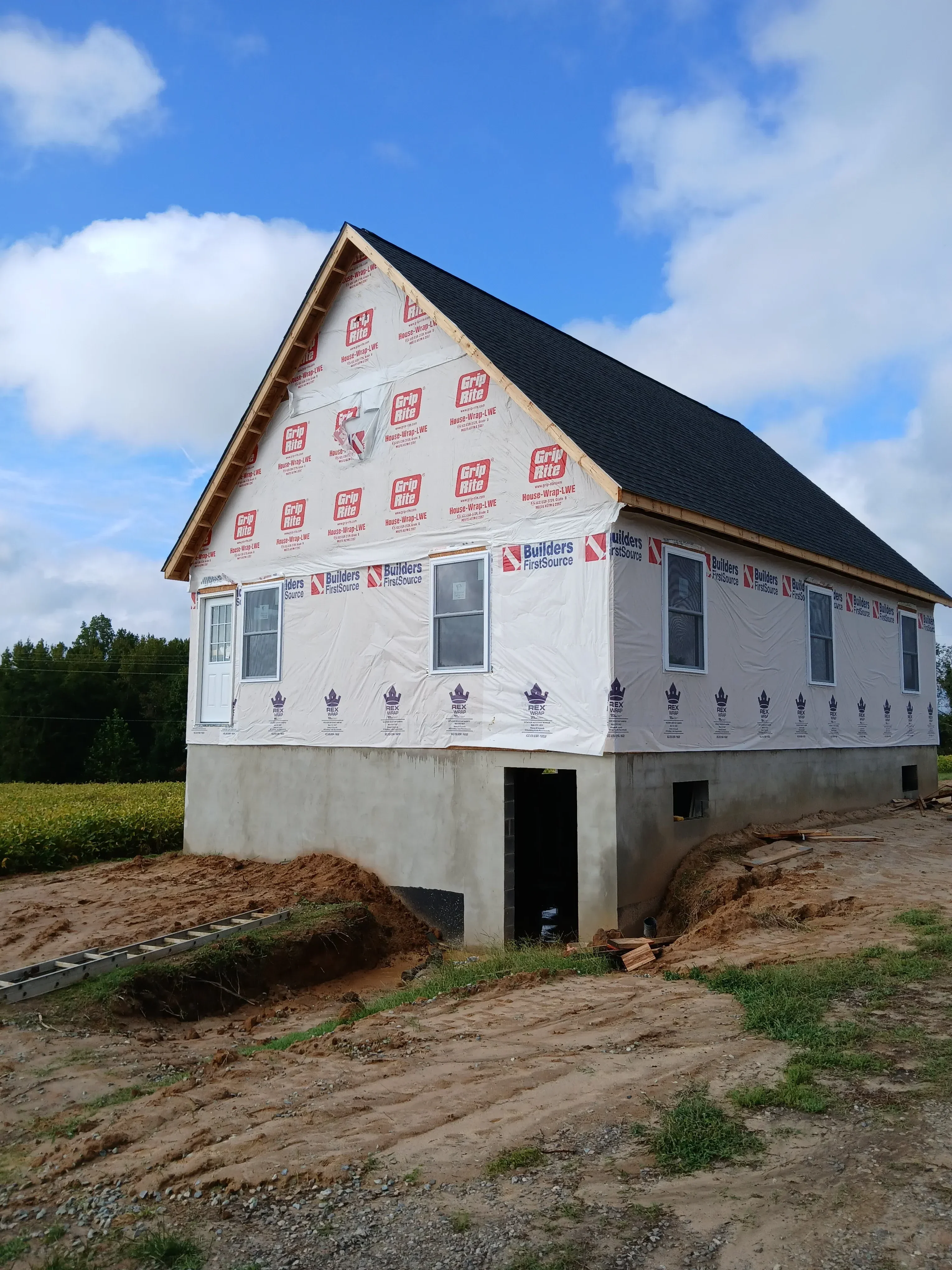 New construction home with white house wrap, window openings, and metal roof installation