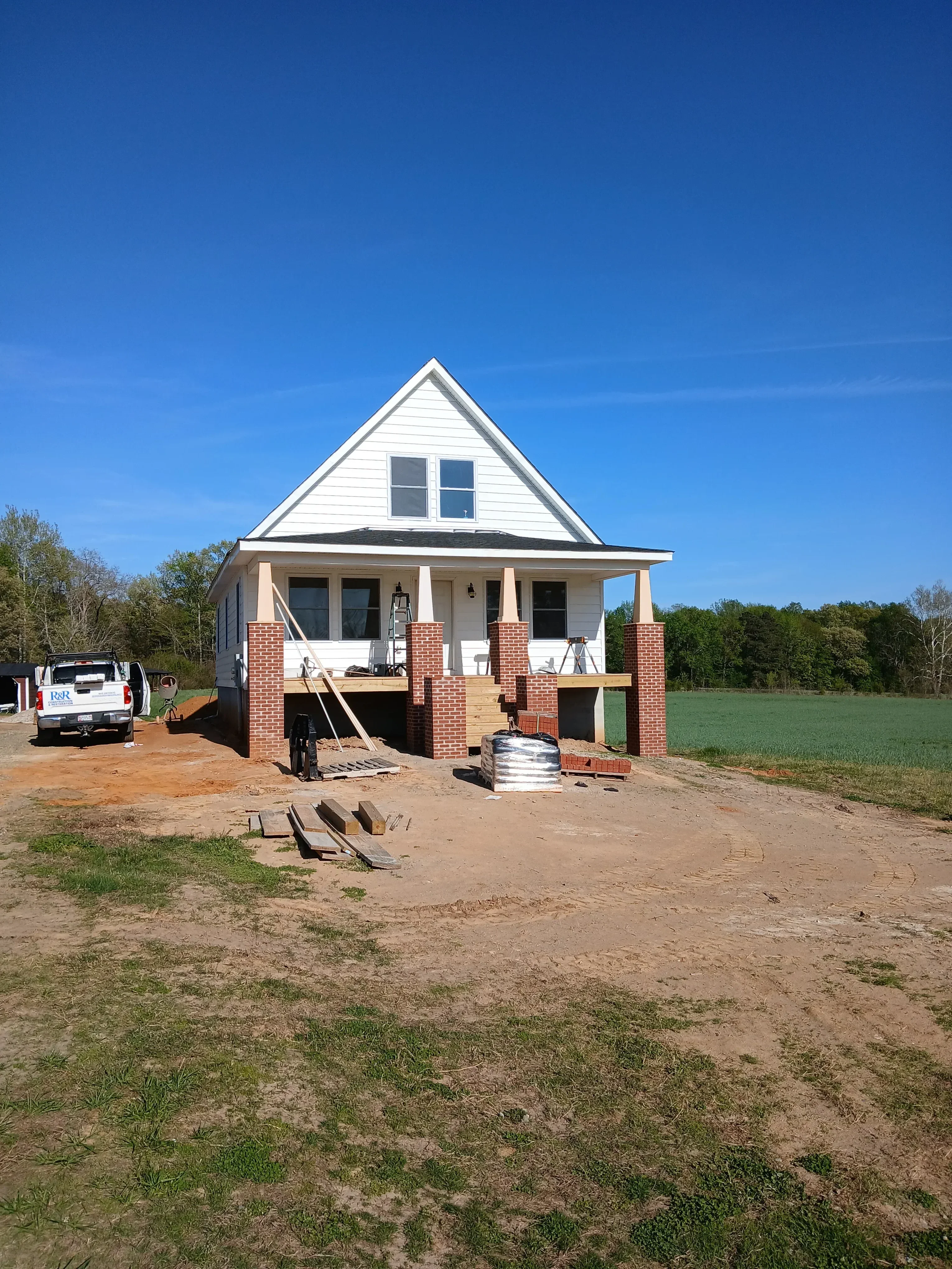 Residential addition with metal roof, red brick chimney, white metal siding, and window installations under construction