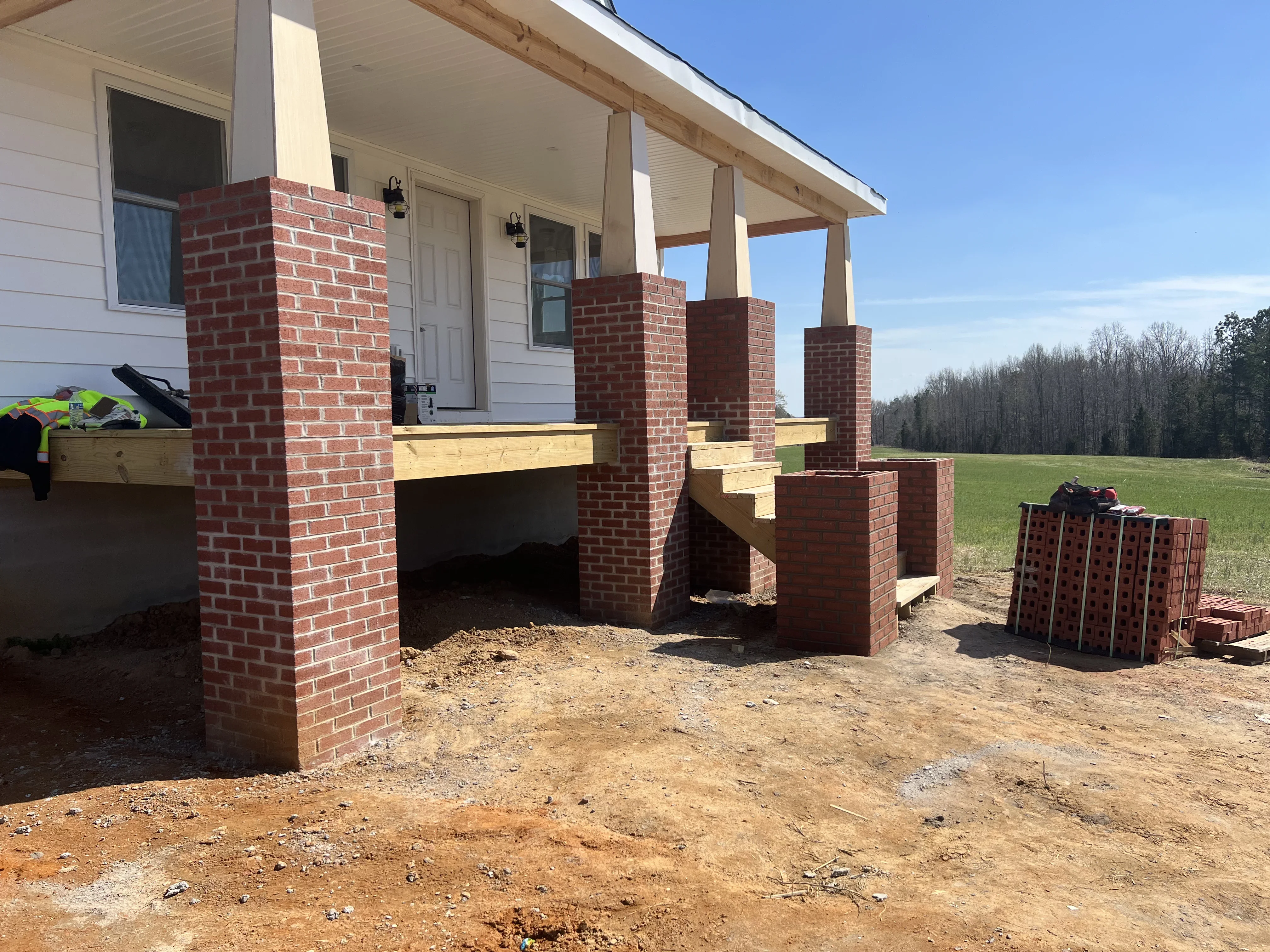 Red brick porch columns with yellow wood beams under construction, attached to residential home