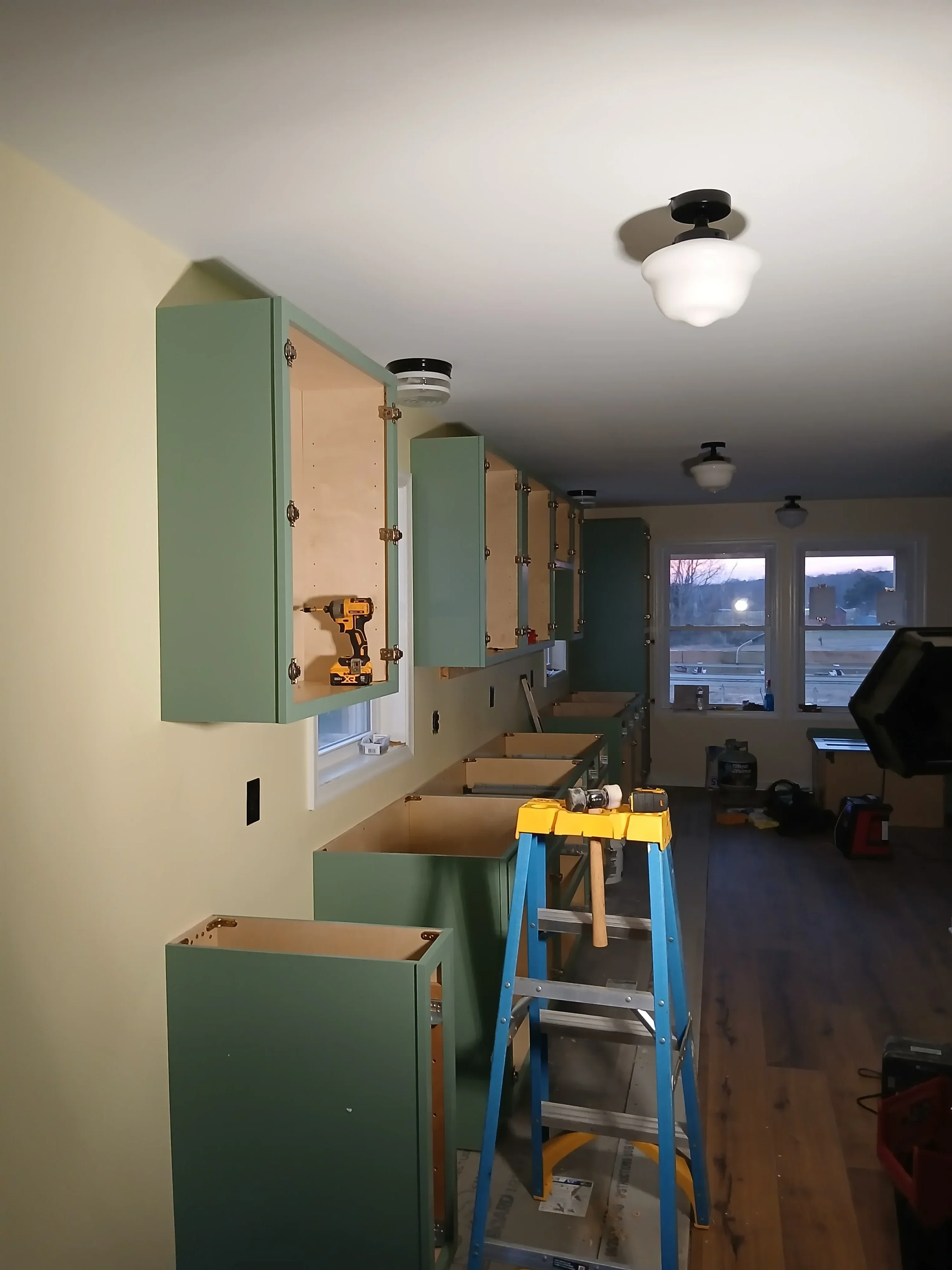 Custom sage green cabinetry with plywood surfaces, wall sconces, and blue structural framing in commercial interior